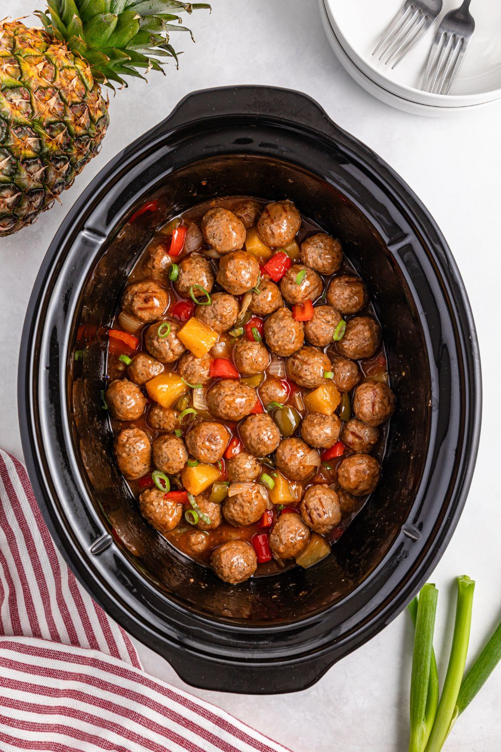 Crock Pot Sweet And Sour Meatballs in a crock pot sitting on table with pineapple and green onions on side of table
