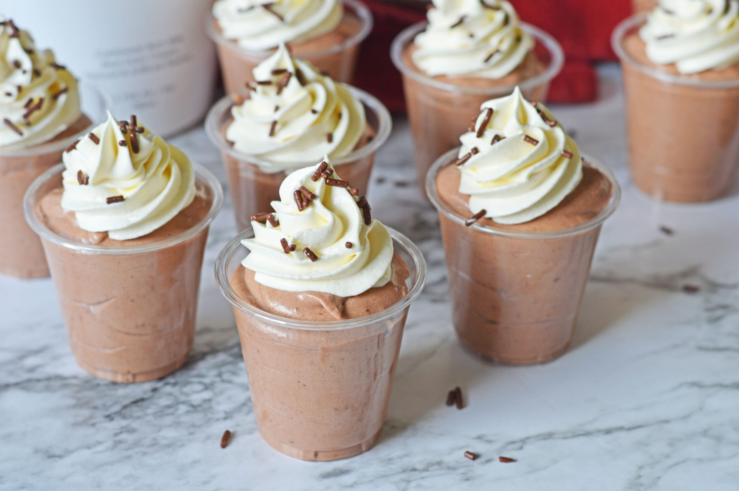 Rumchata pudding shots on a marble table topped with whipped cream and sprinkles