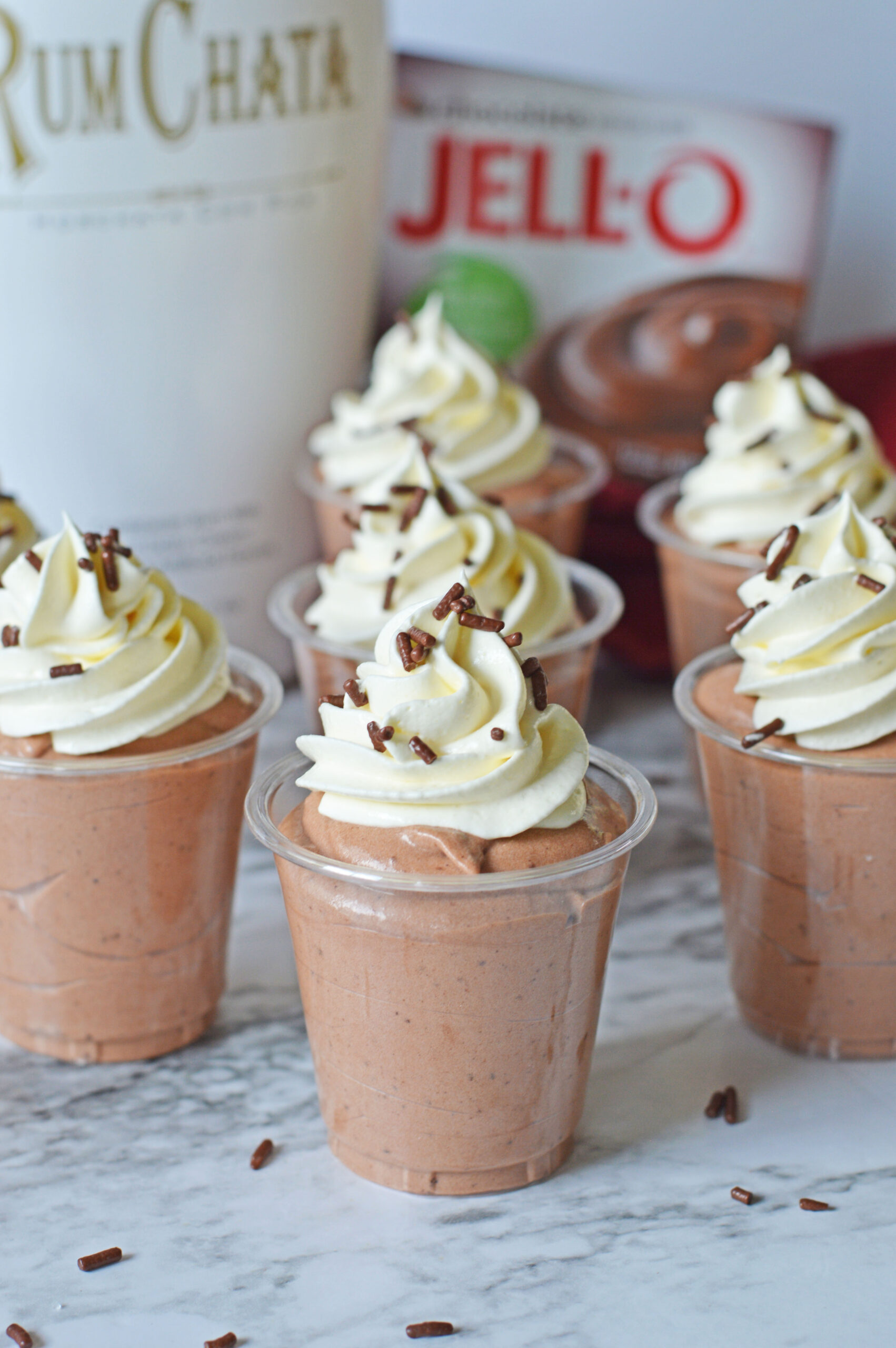 Rumchata pudding shots on a marble table topped with whipped cream and sprinkles