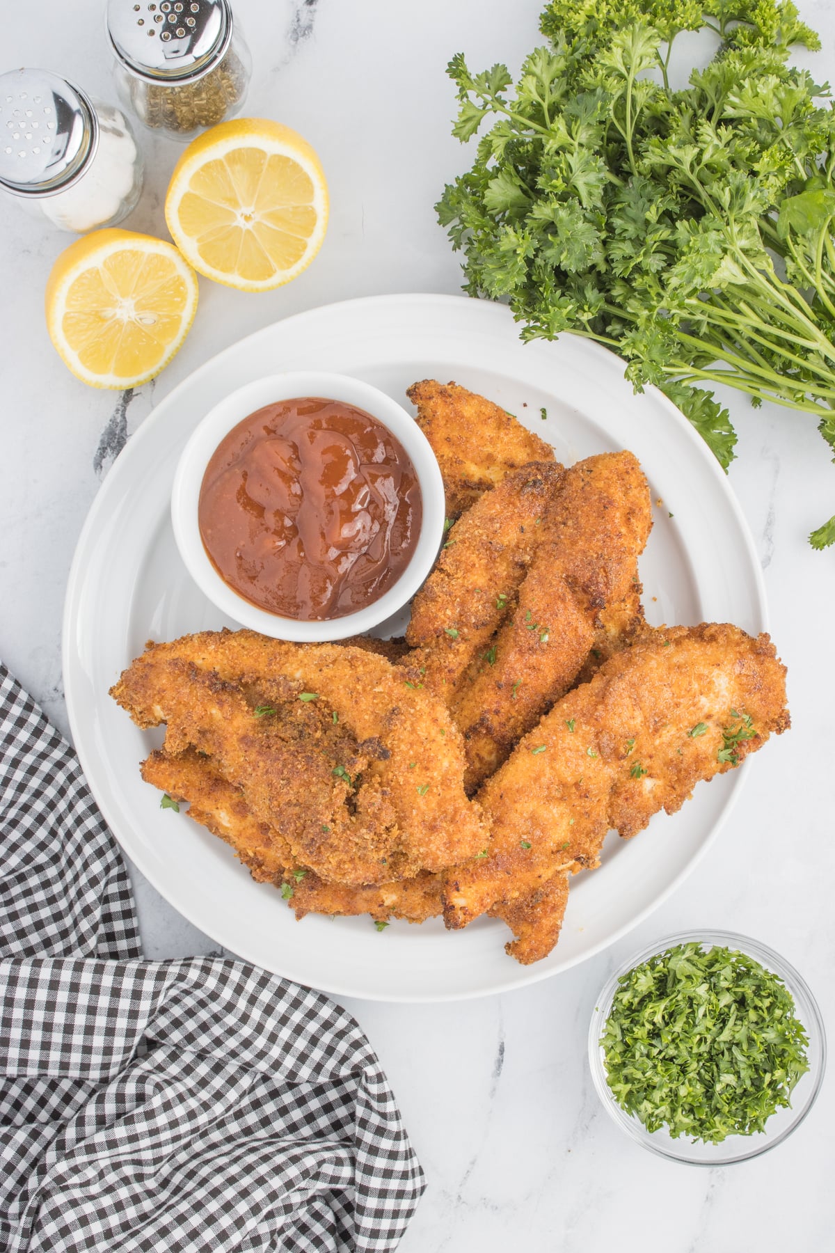 overhead view of Air Fryer Chicken Tenders on a white plate with a small cup of BBQ sauce on the side