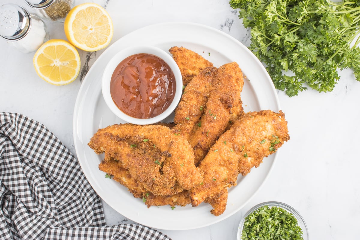 Overhead photo of the Air Fryer Chicken Tenders on a white plate with a small cup of BBQ sauce on the side