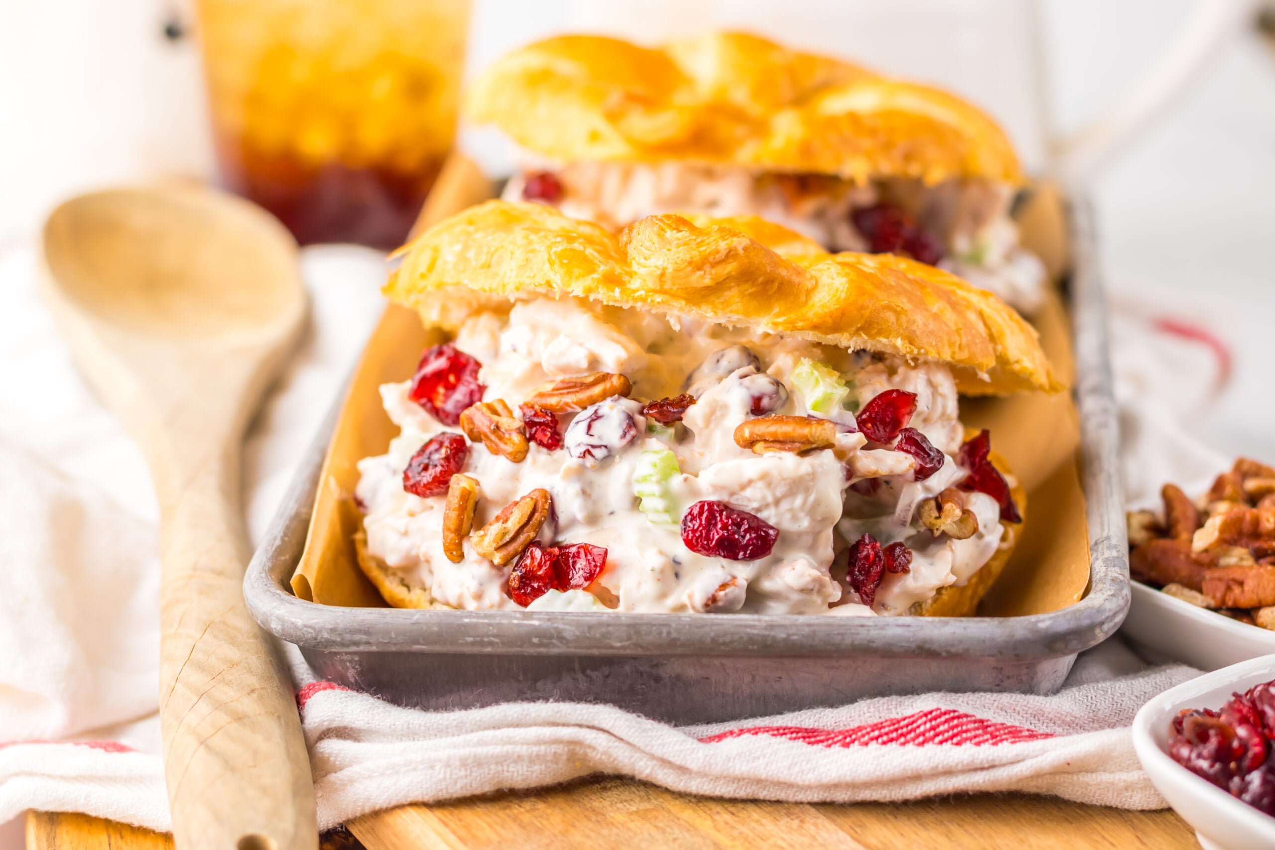 view of a Cranberry Pecan Chicken Salad Croissant on a metal tray sitting on a red and white towel .
