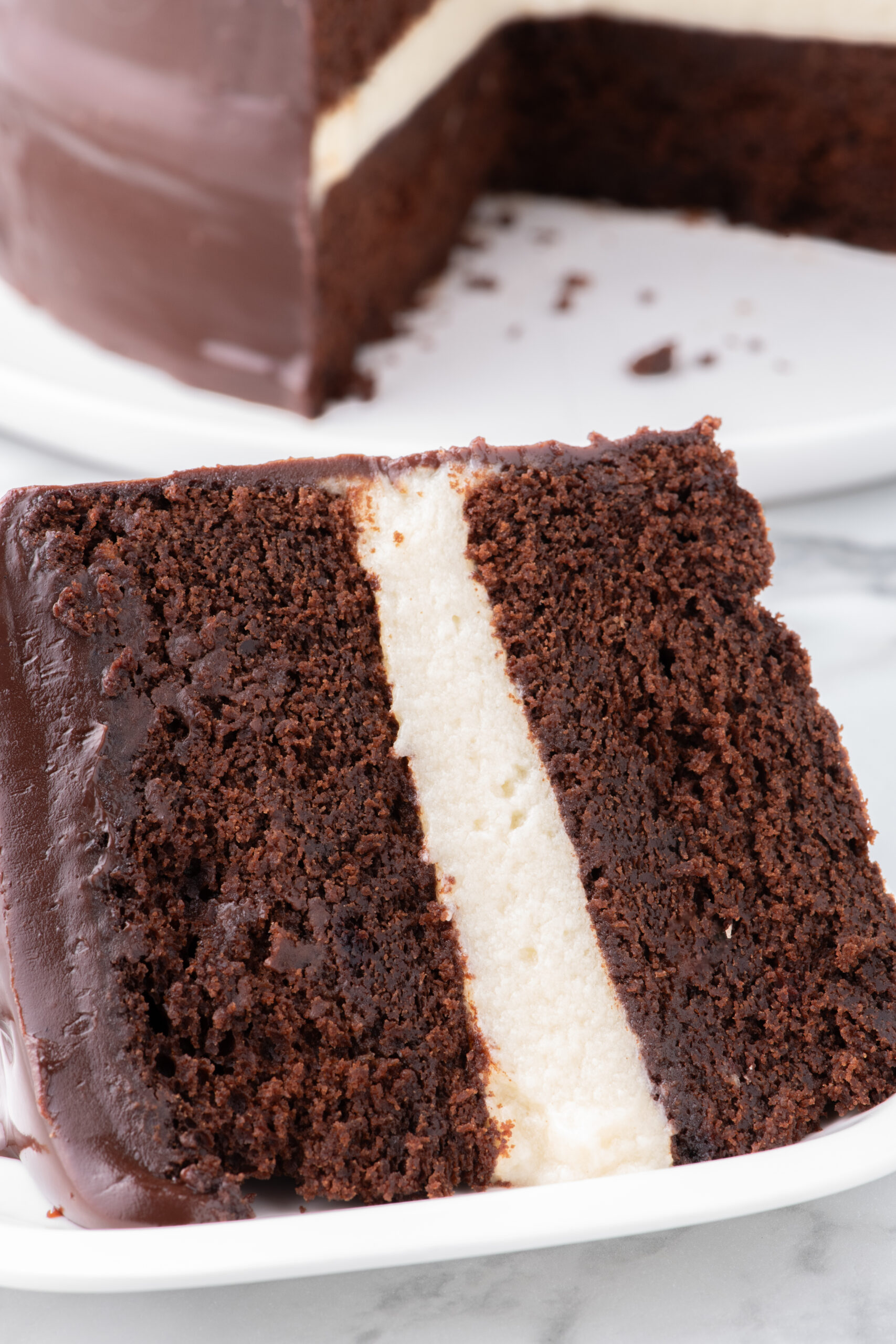 Very close up angle of a Slice of Ding Dong Cake on a white plate with the whole cake in the background