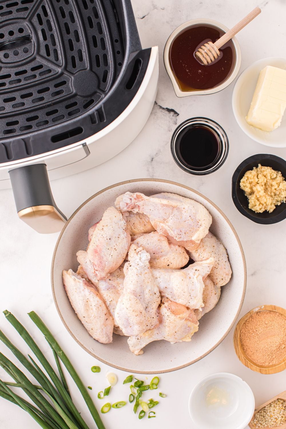 ingredients for Air Fryer Honey Chicken Wings on table in single serve bowls with an air fryer to the side of image 