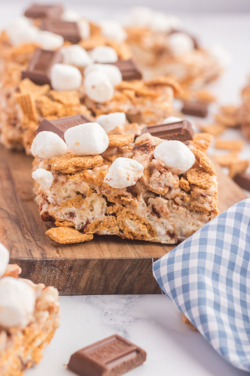 S’mores Rice Krispy Treats on a wooden cutting board with a blue towel in front of it 