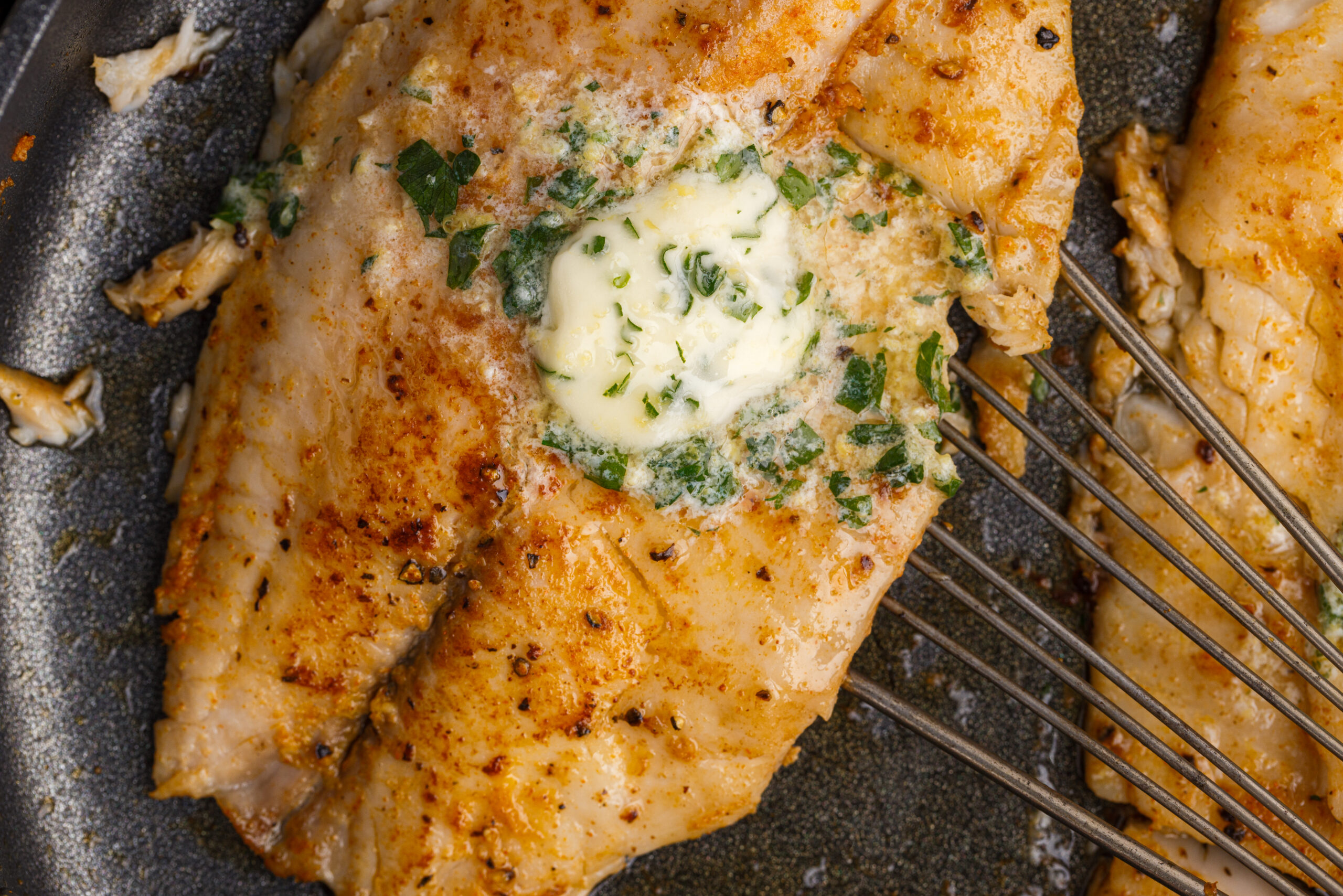 Pan Fried Tilapia in a skillet up close topped with butter