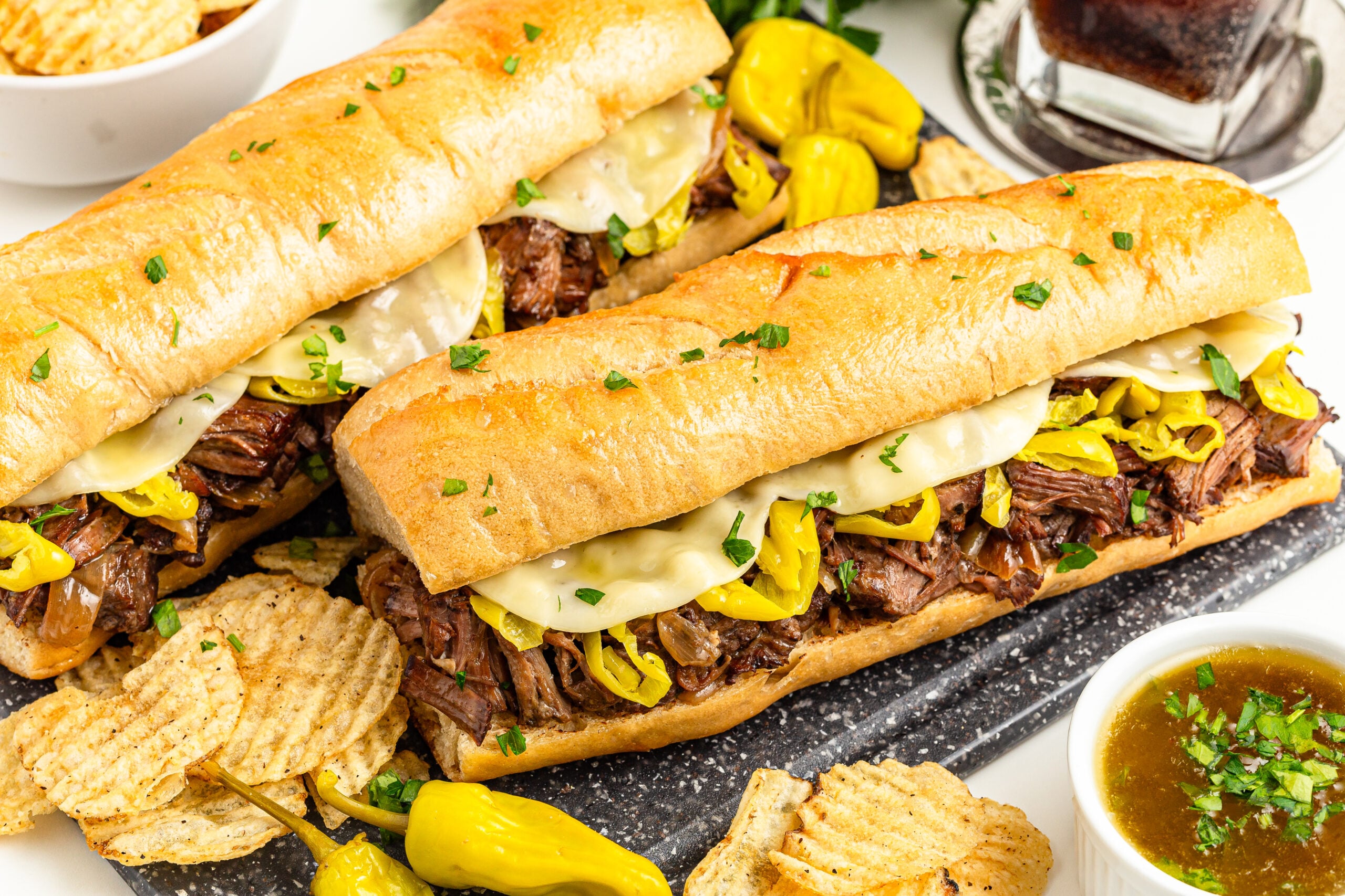 Two Mississippi Pot Roast Sandwiches on a cutting board with chips on the side 
