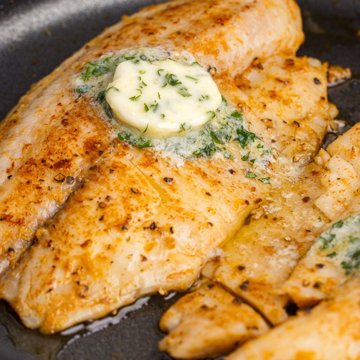 Pan Fried Tilapia in skillet with lemon butter on top