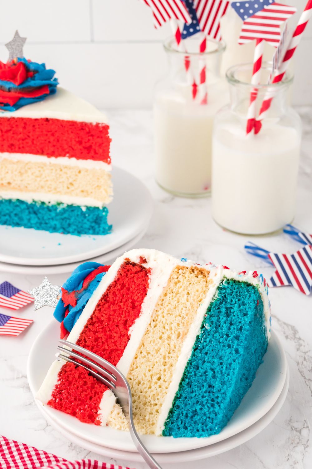 slice of american flag cake on plate with a fork poking in it, and glasses of milk behind it on table