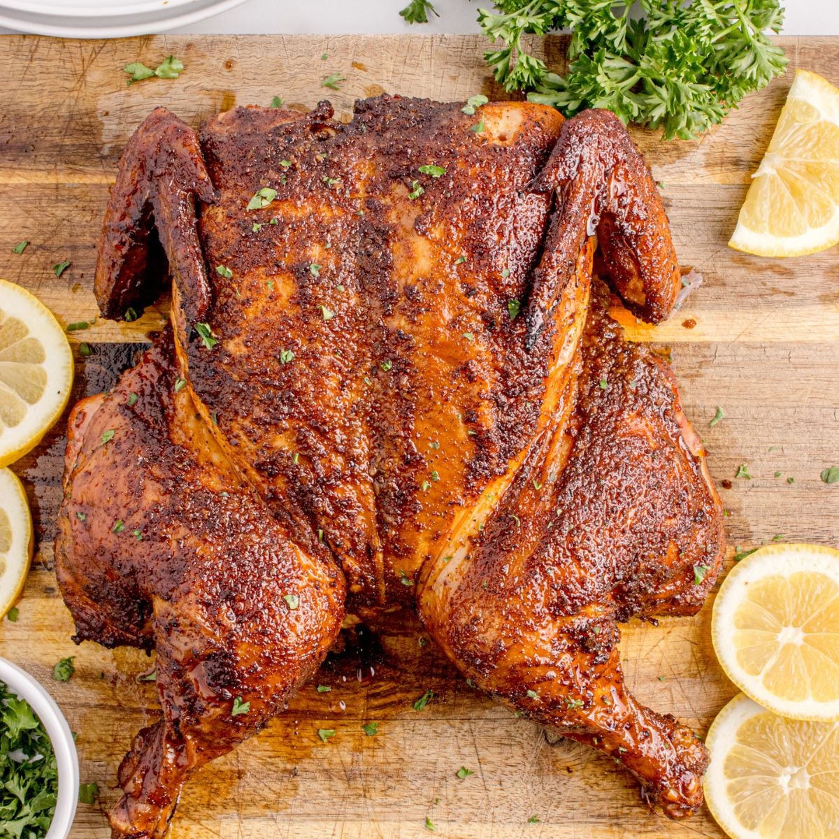Smoked Whole Chicken on a cutting board with lemon wedges to side