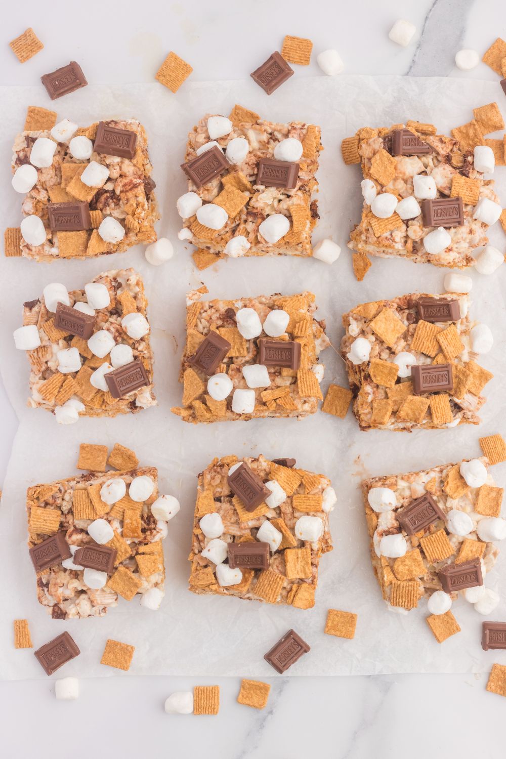 S’mores Rice Krispies cut into squares and placed on table with cereal and chocolate pieces spread on table 
