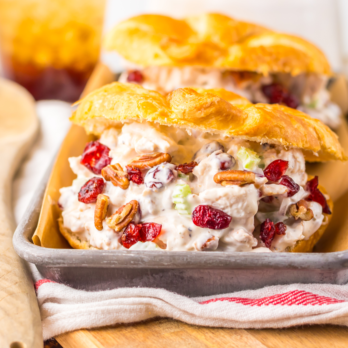 Close up view of a Cranberry Pecan Chicken Salad Croissant on a metal tray sitting on a red and white towel .
