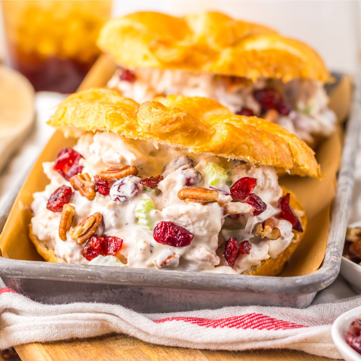 Close up view of a Cranberry Pecan Chicken Salad Croissant on a metal tray sitting on a red and white towel .