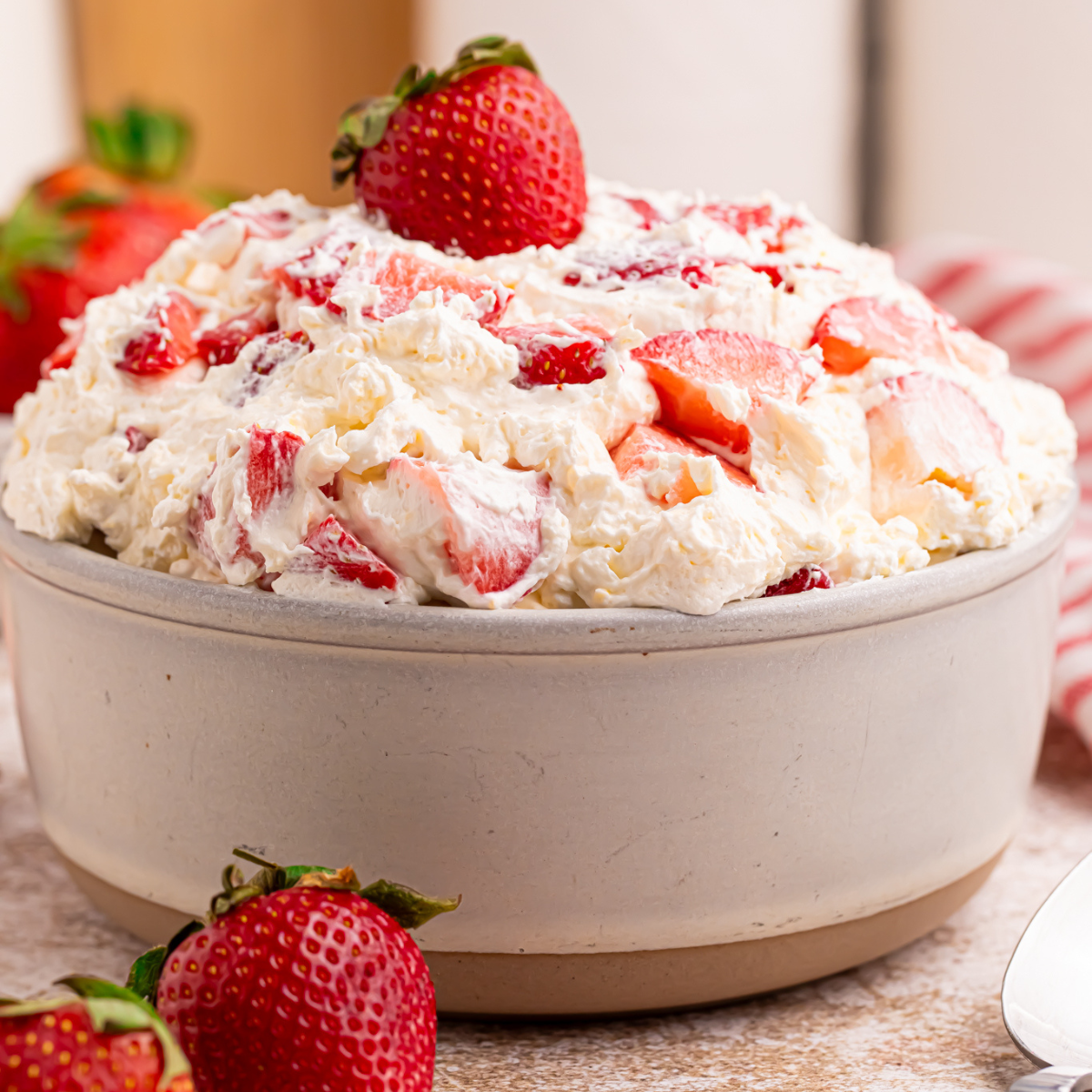 Side view of the strawberry cheesecake salad in a white bowl with a fresh strawberry on top.