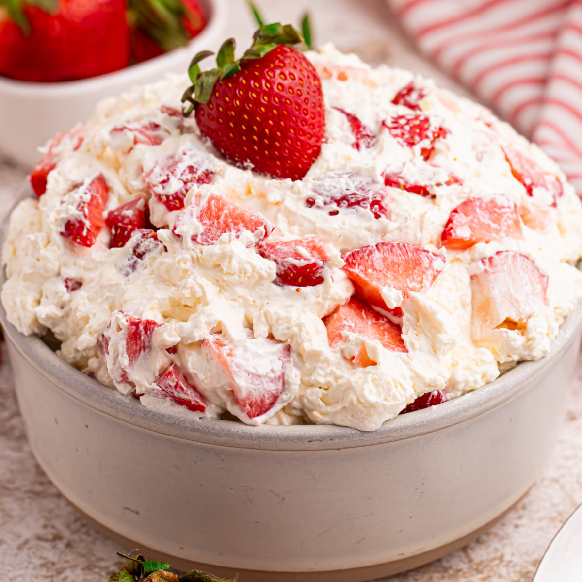 Side view of the strawberry cheesecake salad in a white bowl with a fresh strawberry on top.
