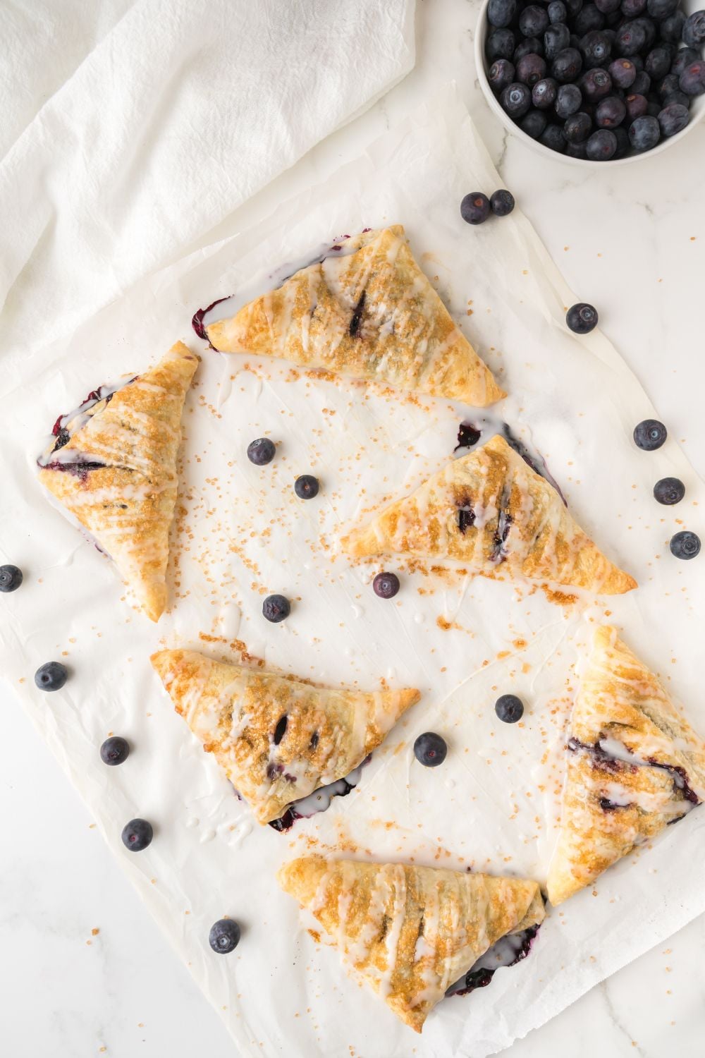 overhead view of Blueberry Turnovers on baking tray with a drizzle of glaze on top