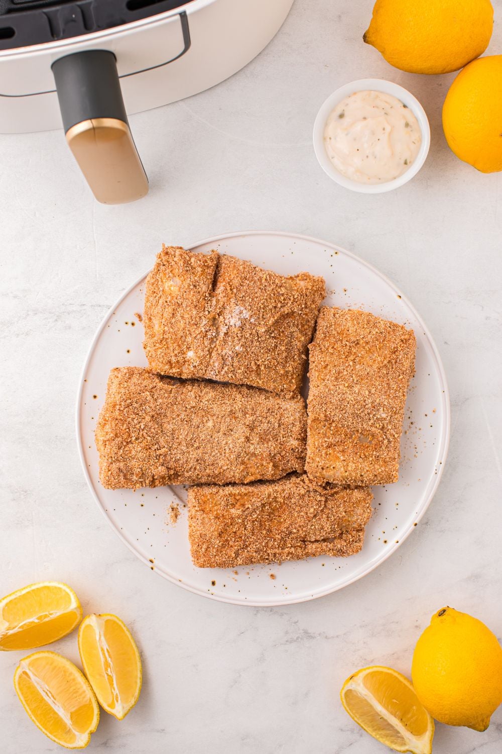 breaded raw fish on a plate with air fryer next to it