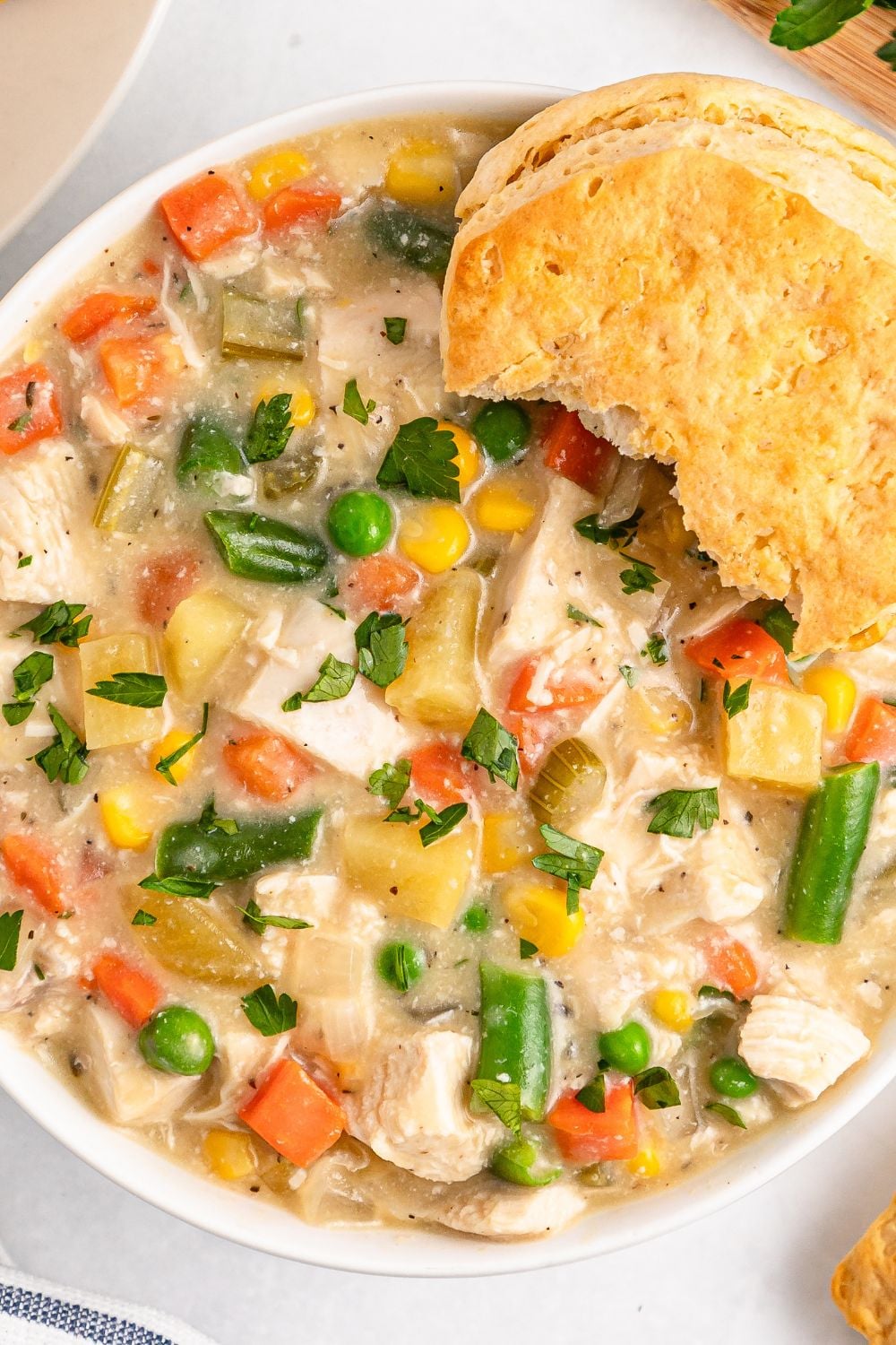 Slow Cooker Chicken Pot Pie in a bowl with some bites taken out of a biscuit on side of bowl 