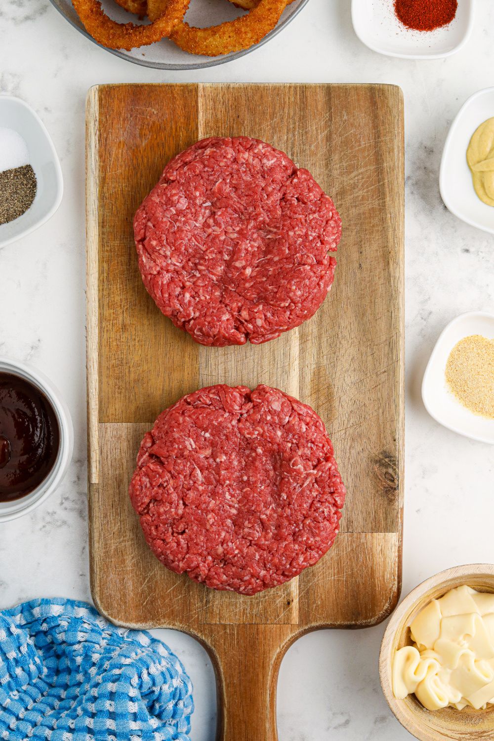 raw hamburger patties on cutting board on table