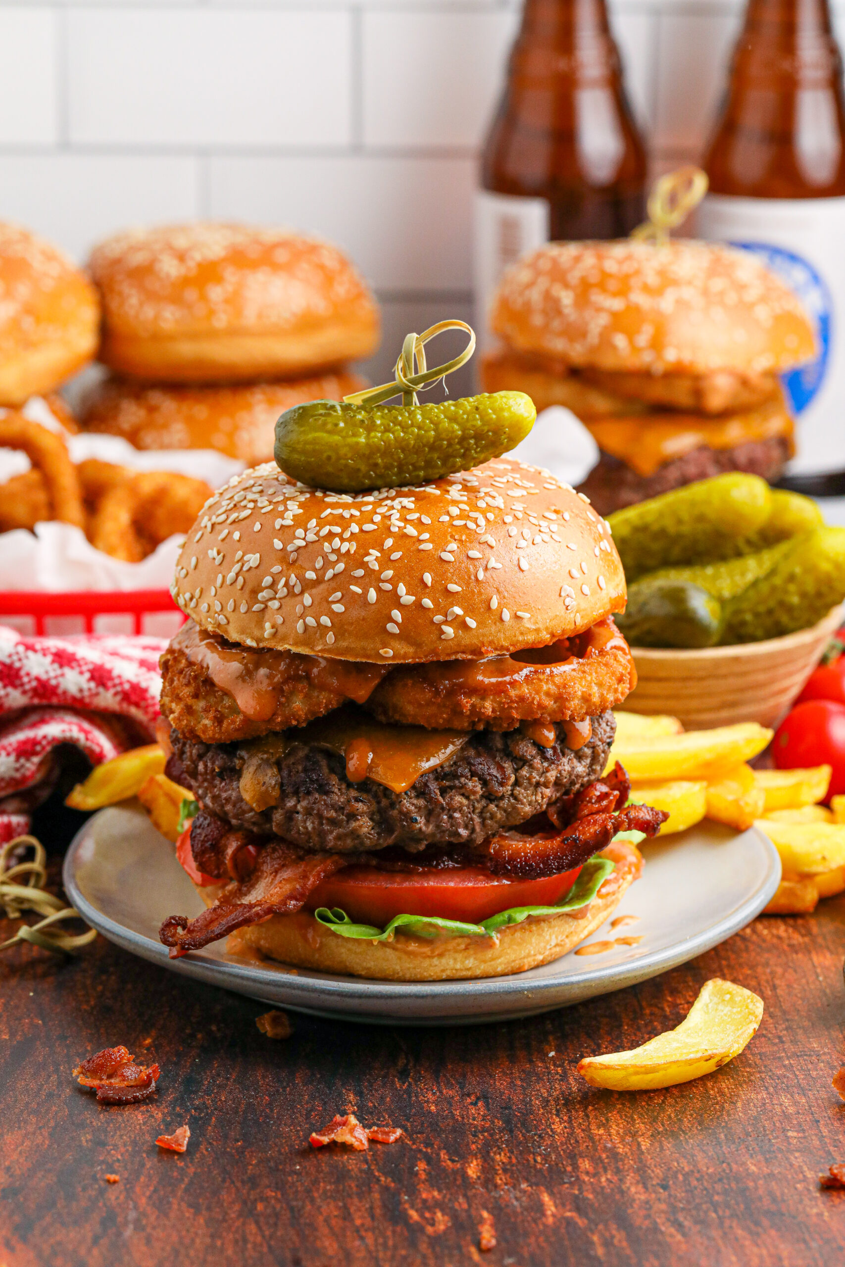 far away shot of the Cowboy Burger on a white plate that is fully loaded with toppings with a small bowl of pickles and fries in the background