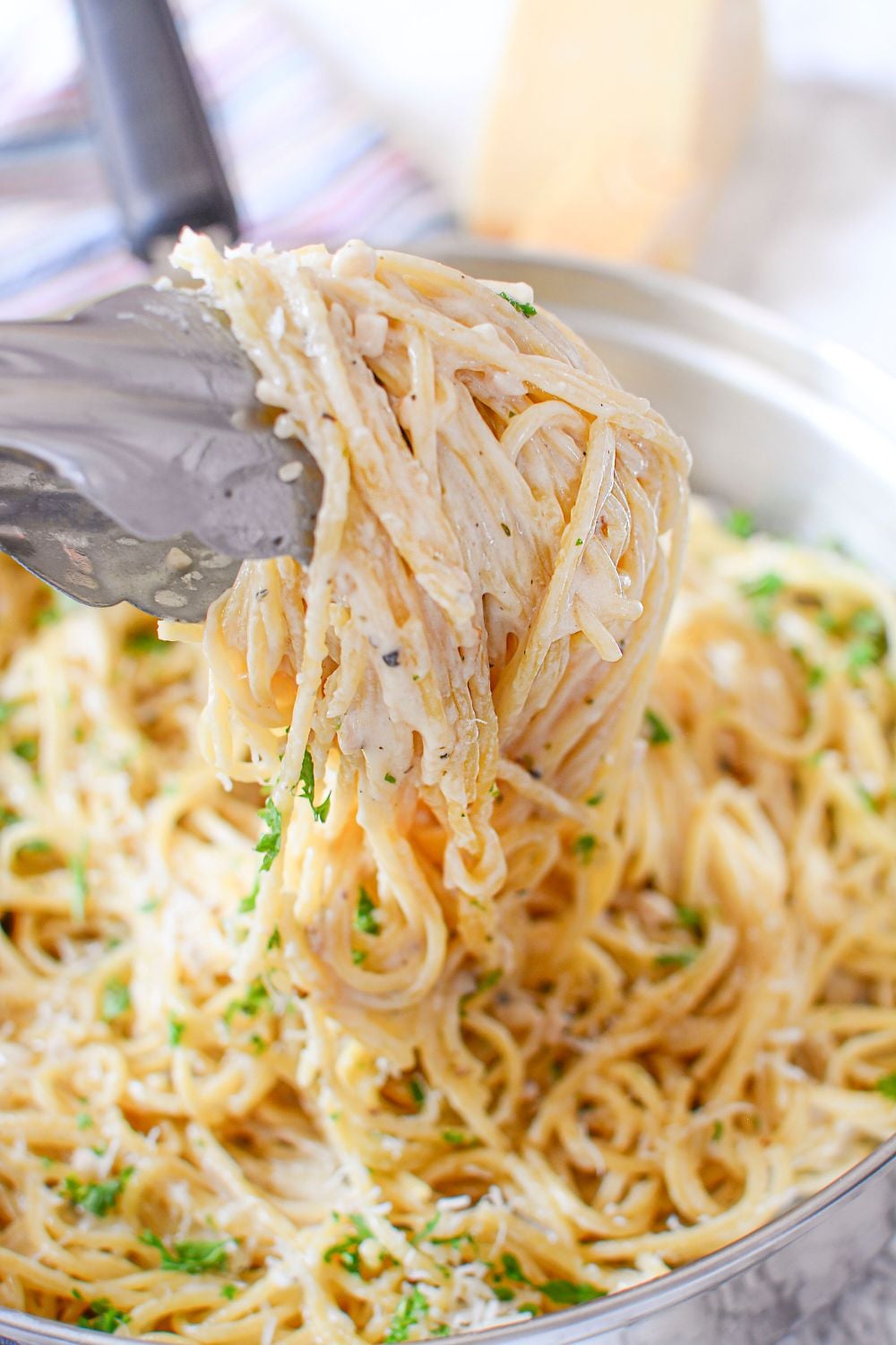 garlic parmesan pasta on tongs being lifted out of skillet