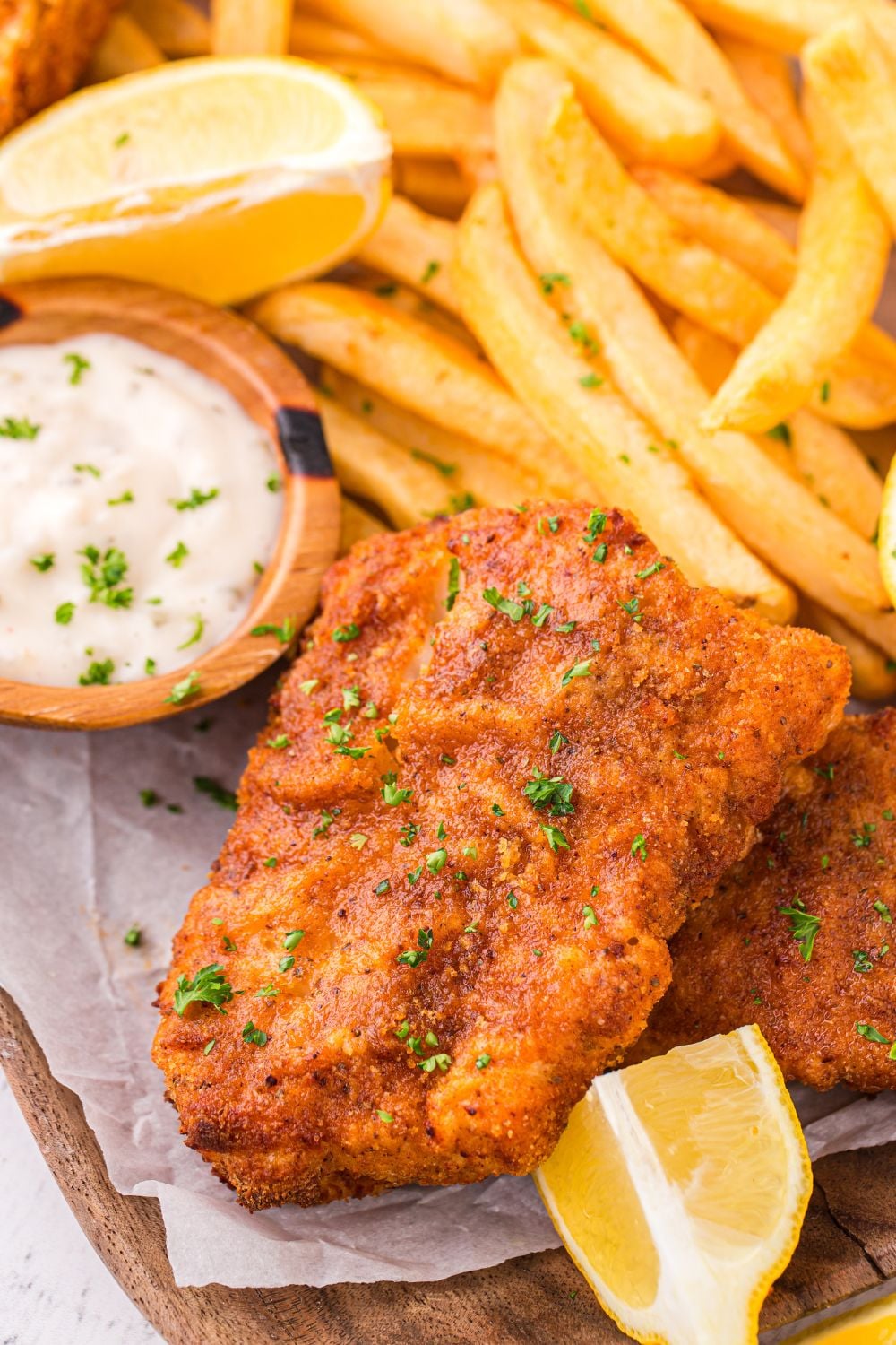 Air Fryer Fish And Chips on a table with some parchment paper under it with lemon wedges and tartar sauce