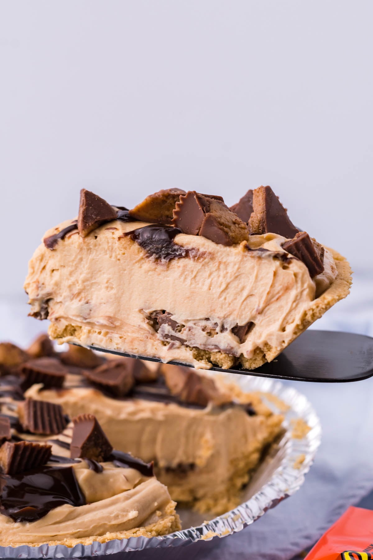 A side view of a slice of no bake peanut butter cup pie being removed from the pan with a black spatula.