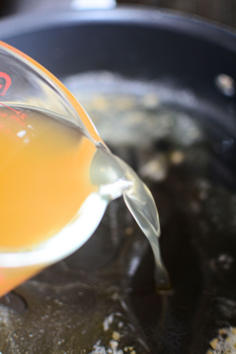broth being poured into skillet with sauteed garlic in pan