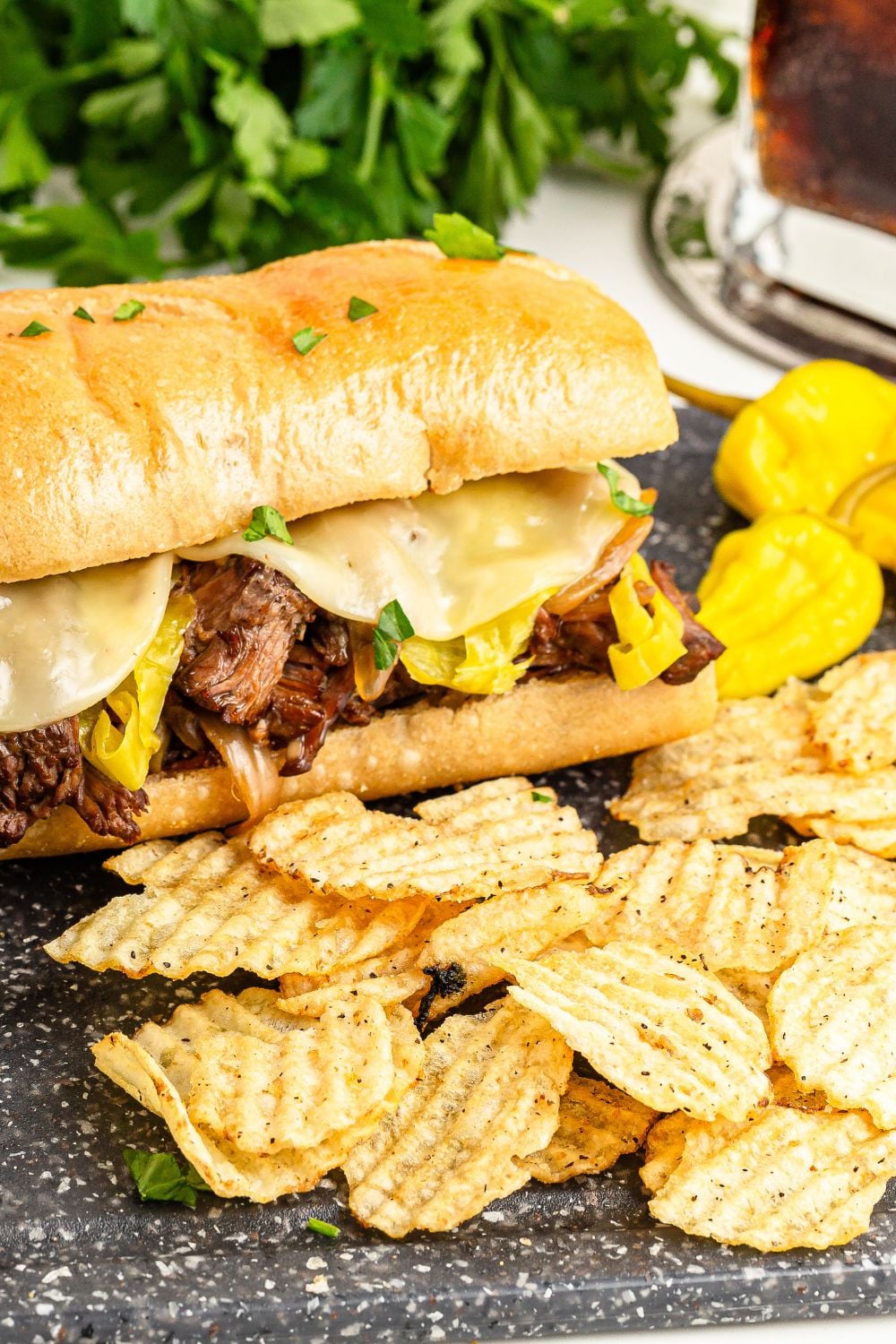 Mississippi Pot Roast Sandwich on table with some chips and peppers to the side of sandwich 
