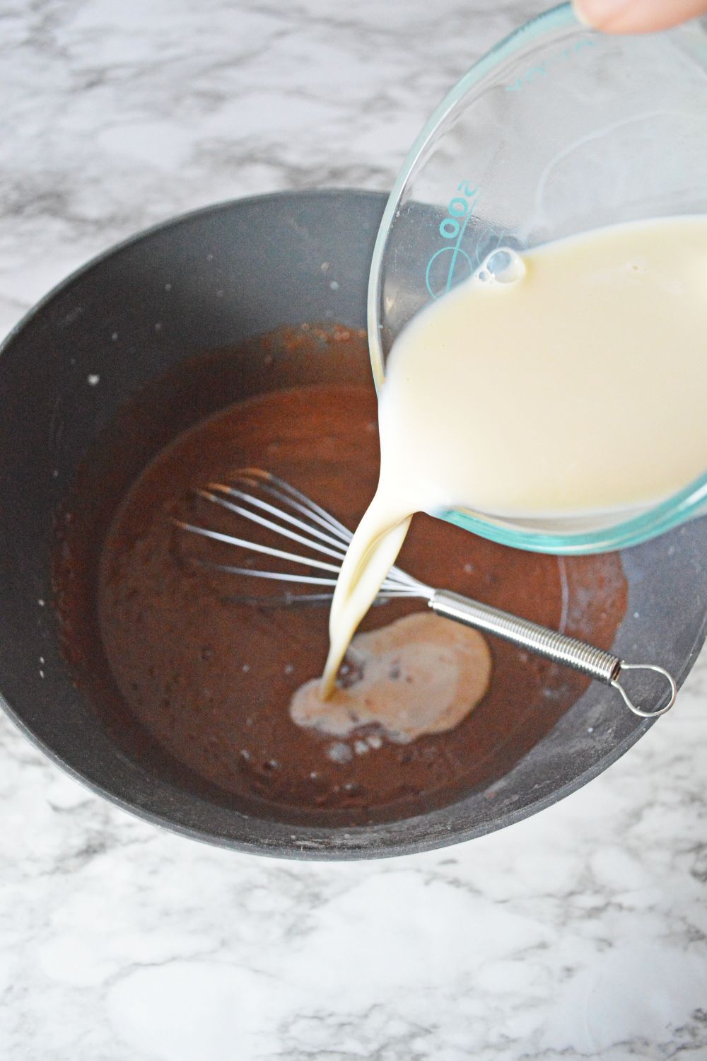 milk being poured into chocolate pudding mixture in bowl 