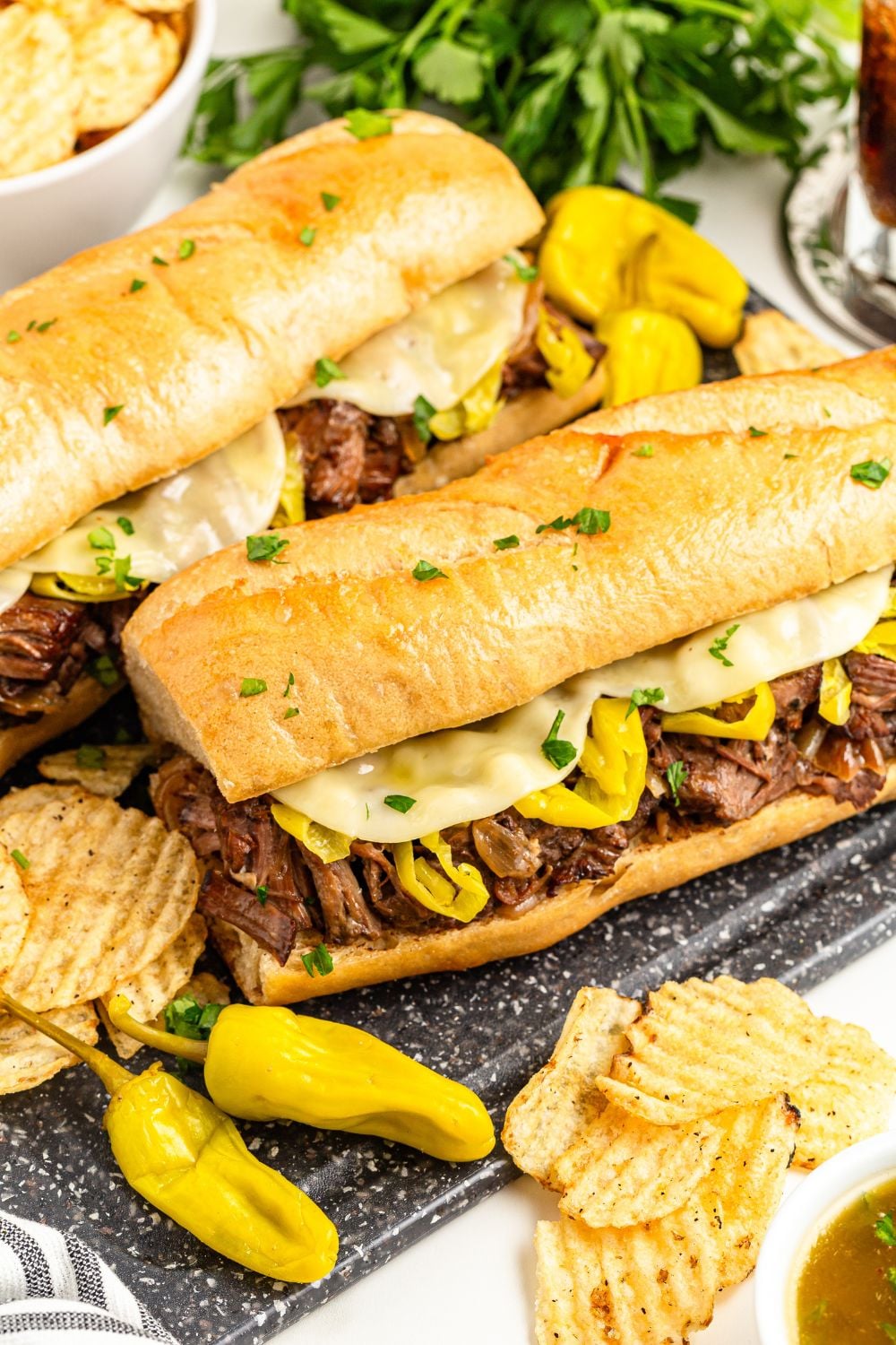 mississippi beef sandwiches and peppers on table with some chips and a bowl of au jus on side