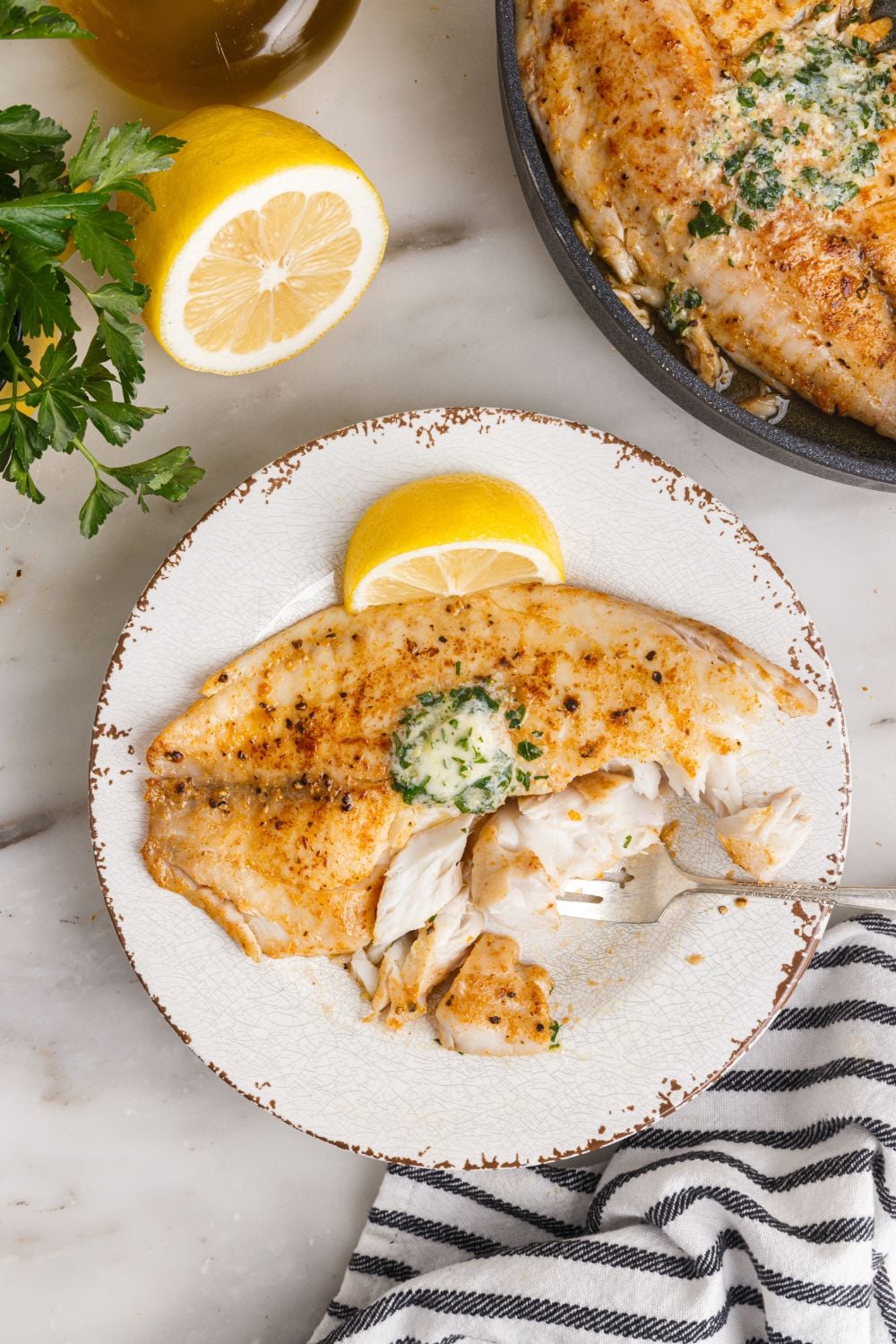 Pan Fried Tilapia on plate with pan of fish to side and lemons to showcase on side of plate