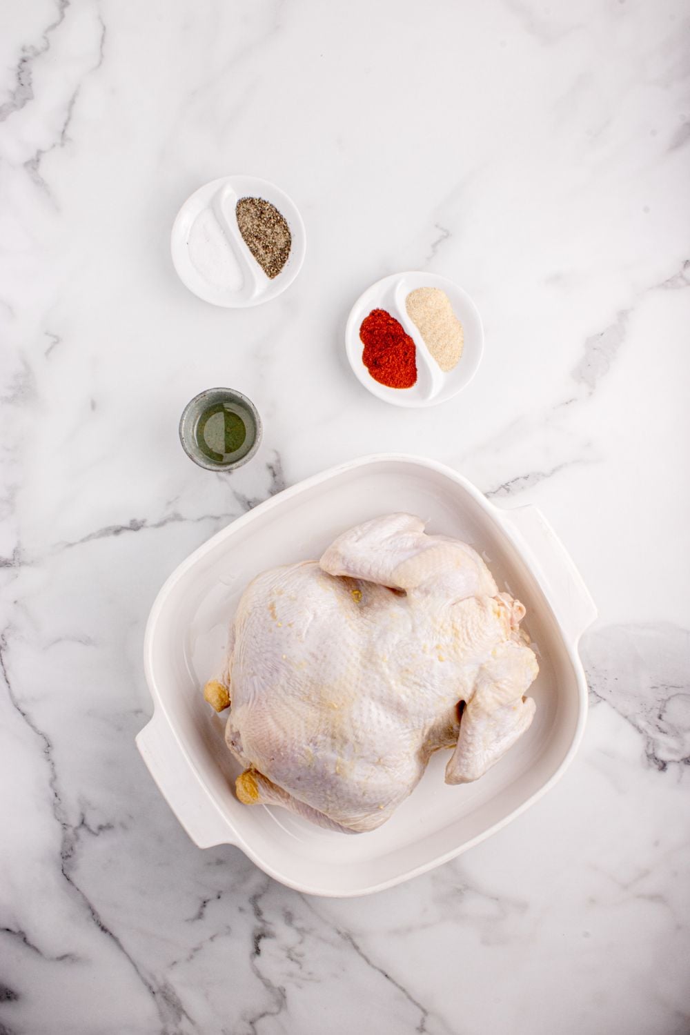 raw whole chicken on table with bowls of spices to side in single serve bowls