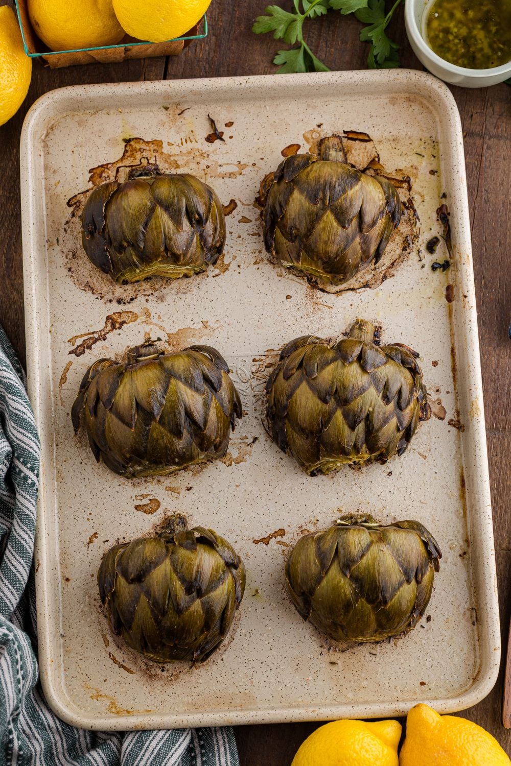 oven roasted artichokes on a baking tray with lemons around it
