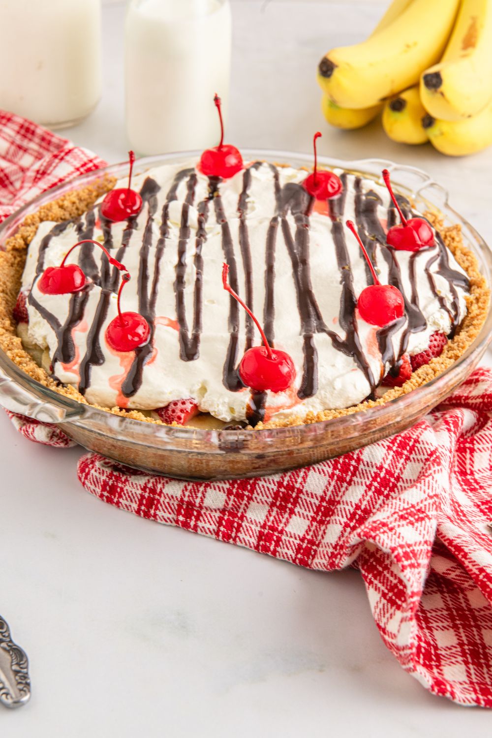 No Bake Banana Split Pie on table with glasses of milk to side and bananas behind the pie