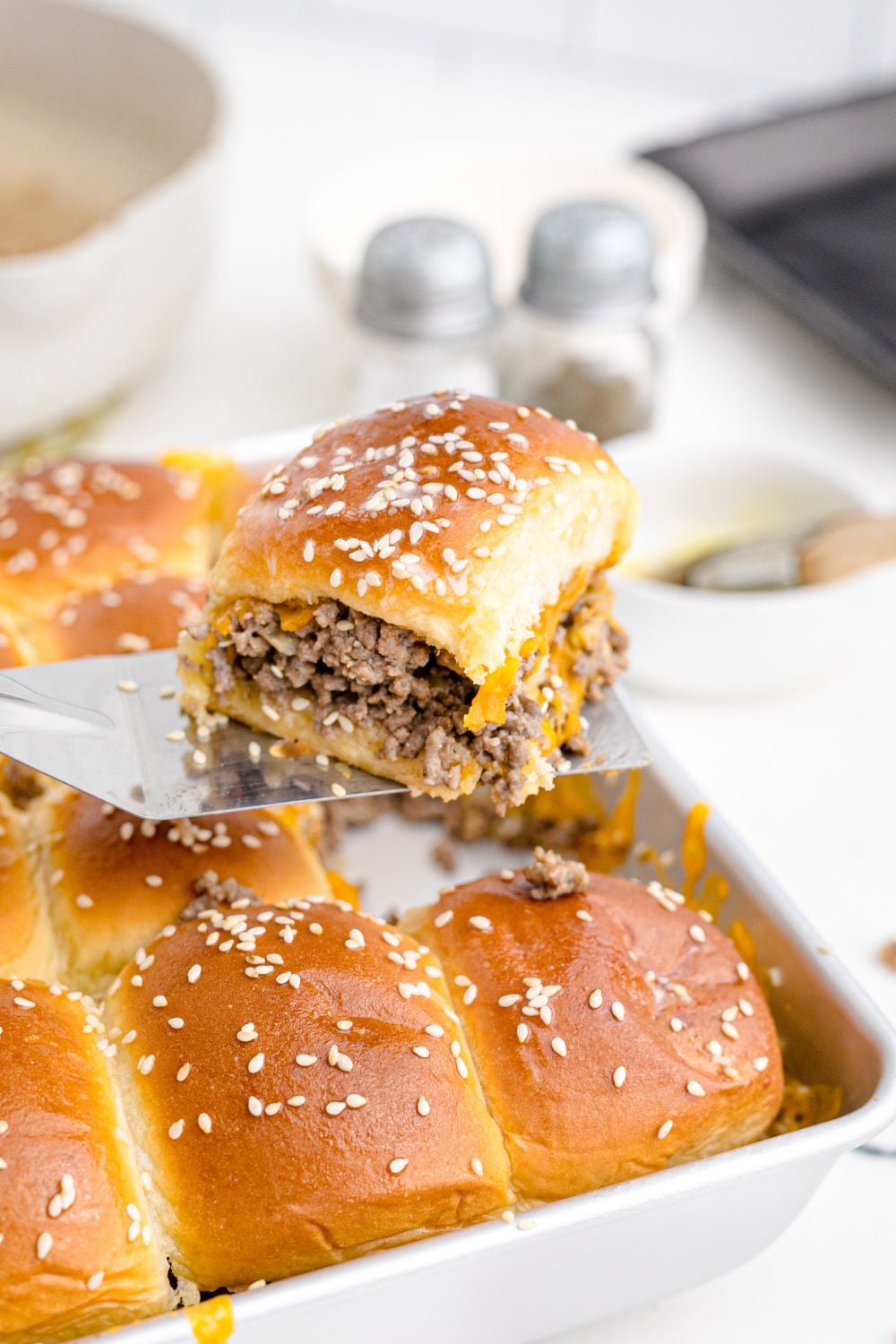 Beef and cheese sliders in a pan with one getting lifted out of pan