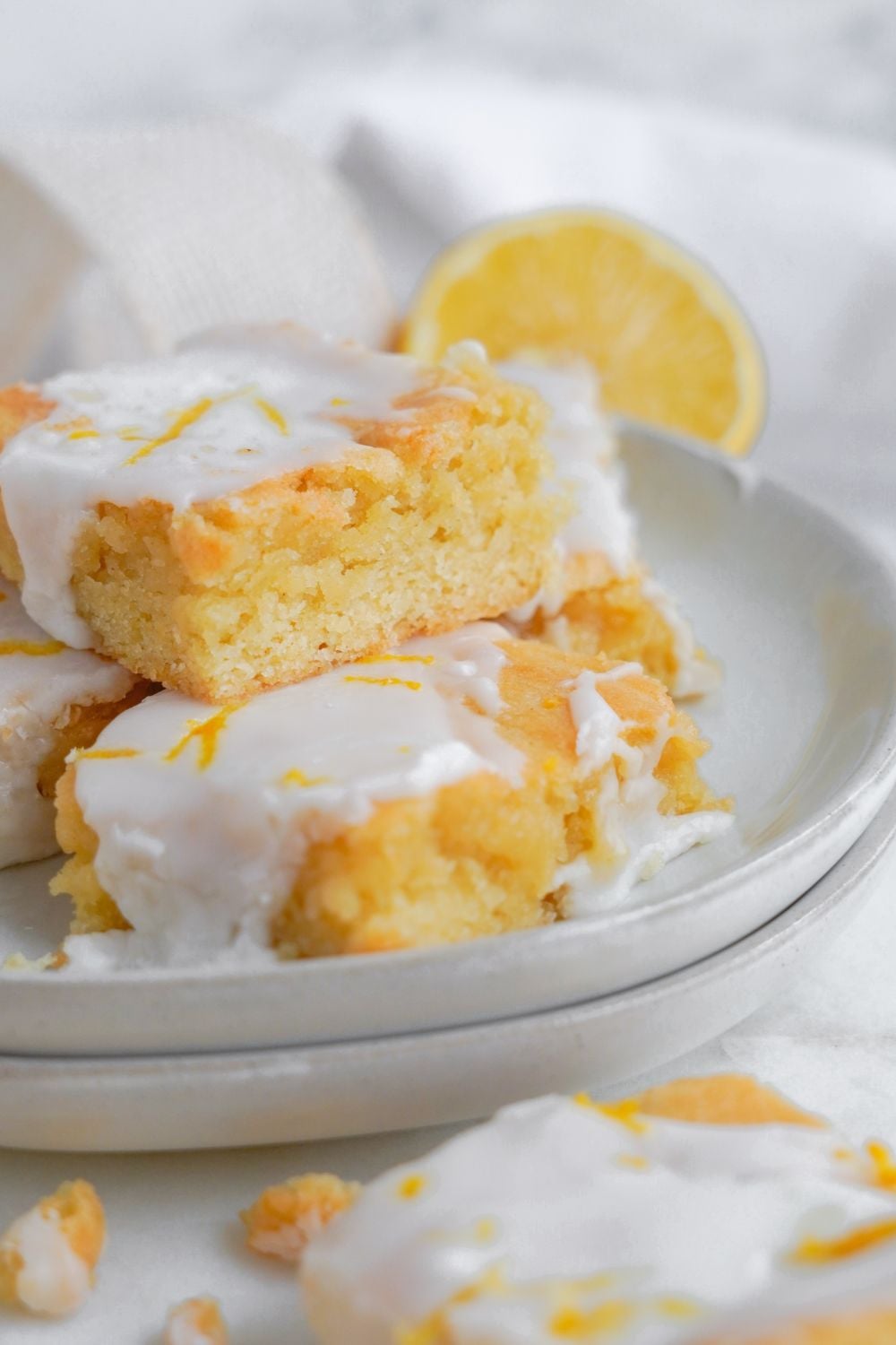 Lemon Sugar Cookie Bars stacked on a platter and a lemon sliced in half sitting on table to the side of bowl