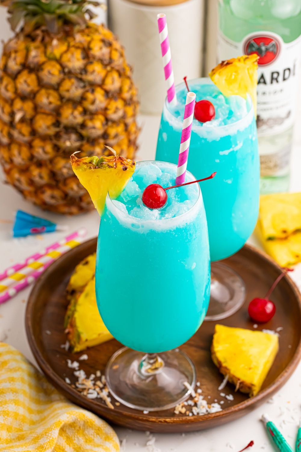 Frozen Blue Hawaiian Cocktails in glasses on table with a whole pineapple in background and sliced pineapple around table 