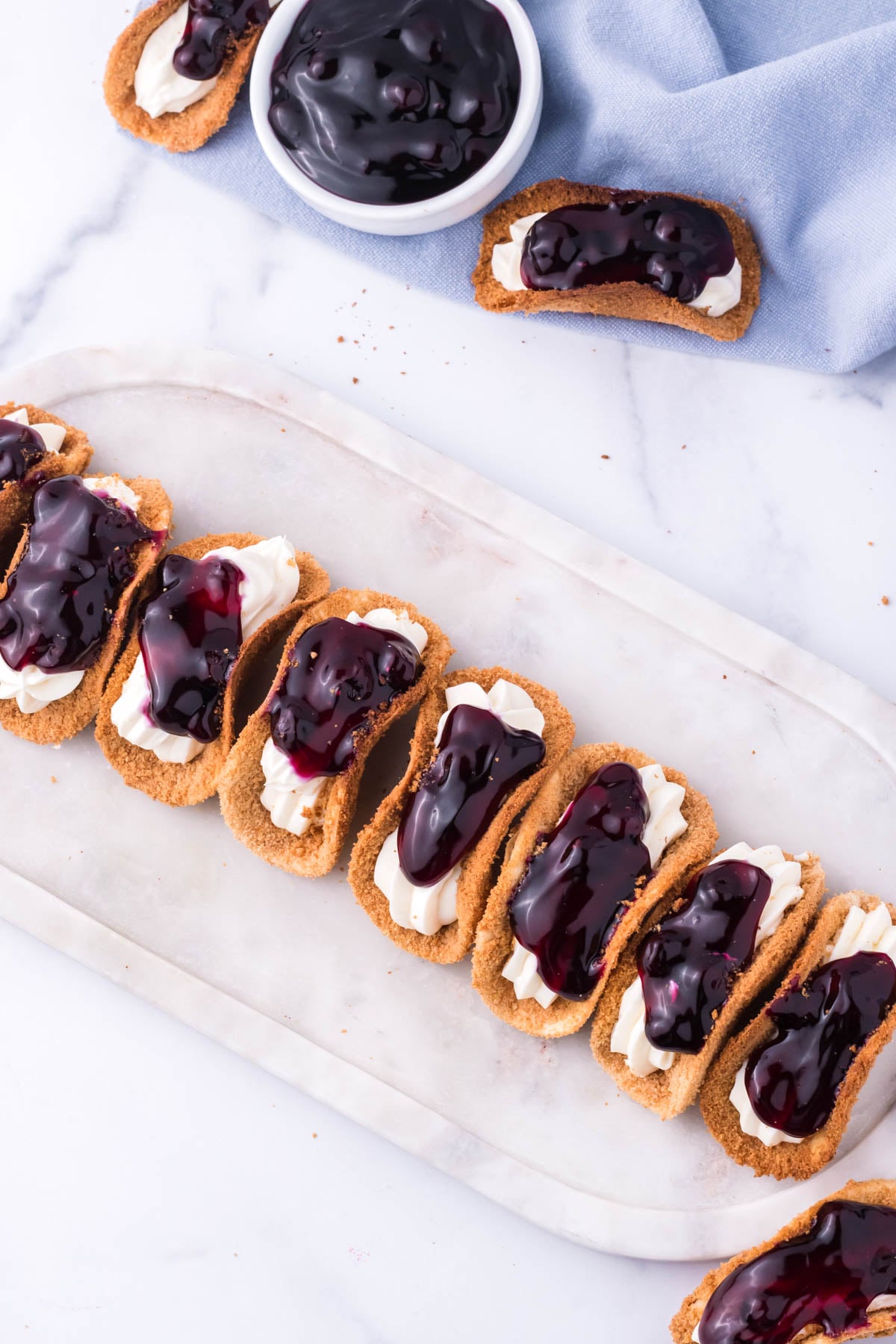 Overhead view of blueberry cheesecake tacos lined up on a marble serving platter.