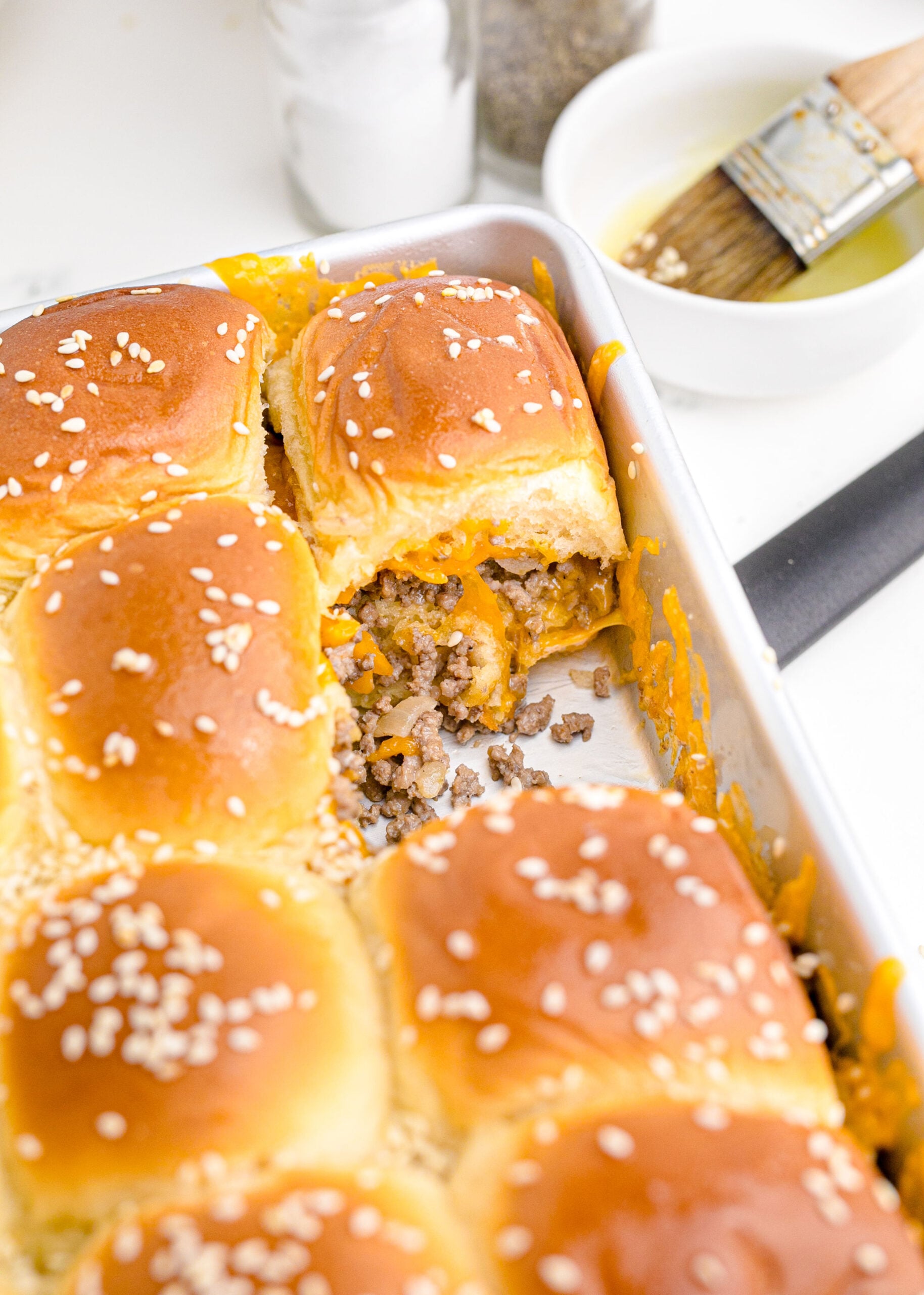 A baking pan full of the cheeseburger sliders with a one missing