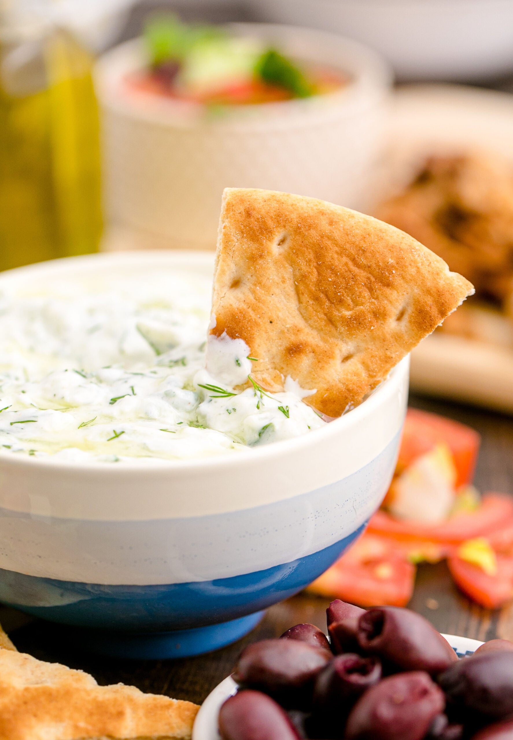 Tzatziki Sauce in a white and blue bowl with a pita chip sticking out of it