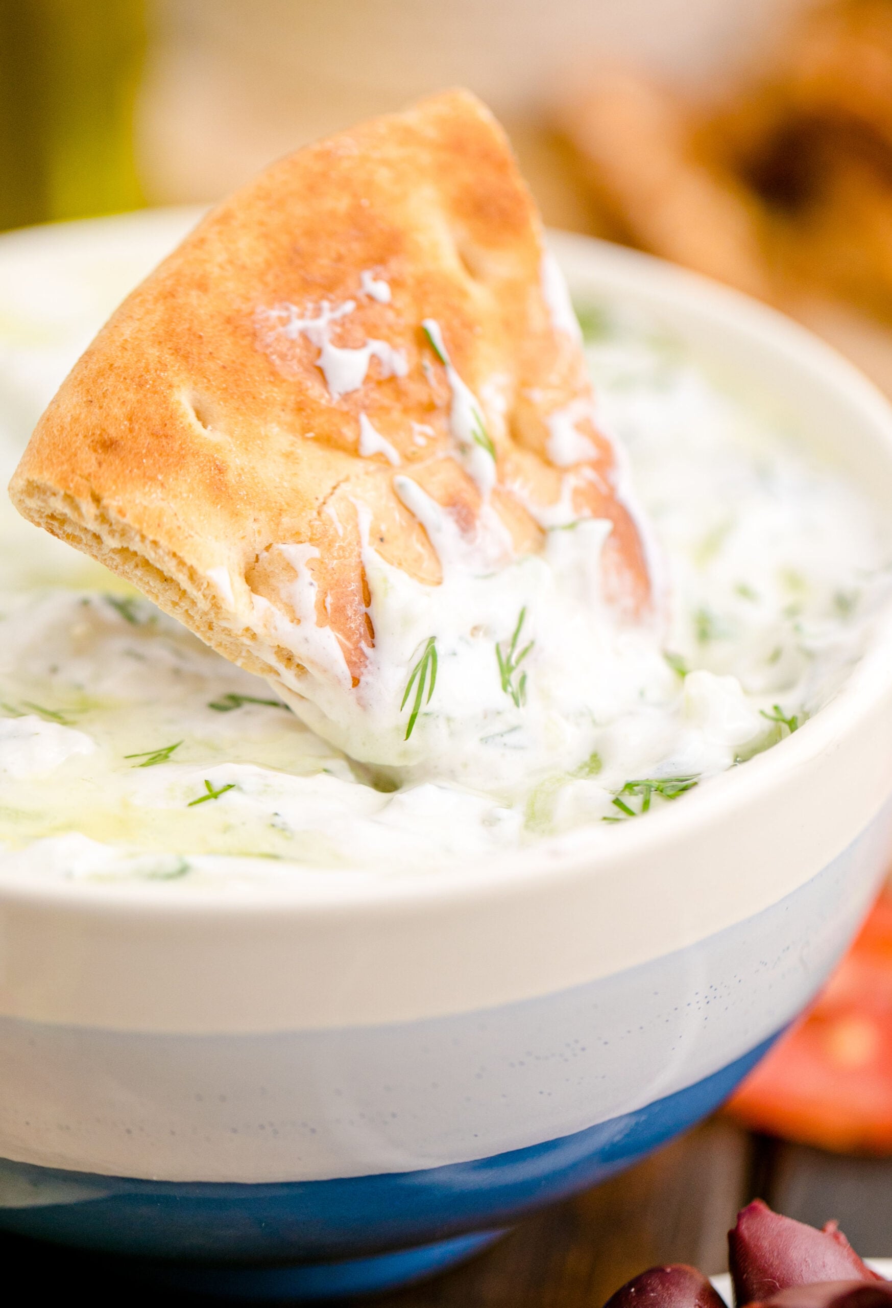 Tzatziki Sauce in a white and blue bowl with a sauce covered pita chip being dipped in