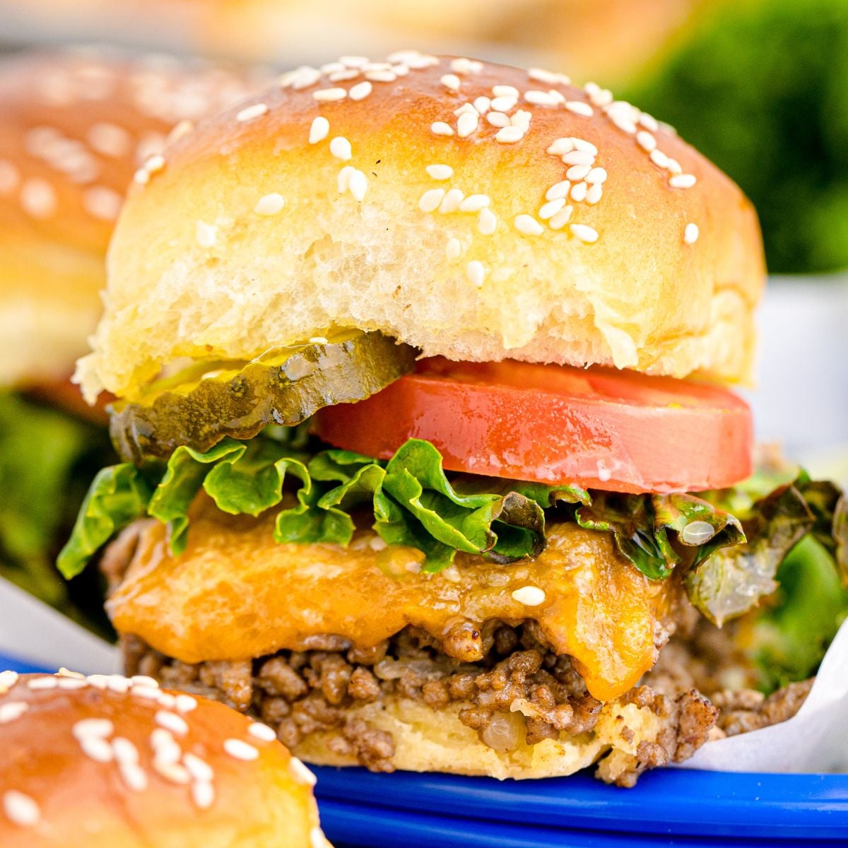 Classic Cheeseburger Sliders in a blue basket on table with more burgers around it