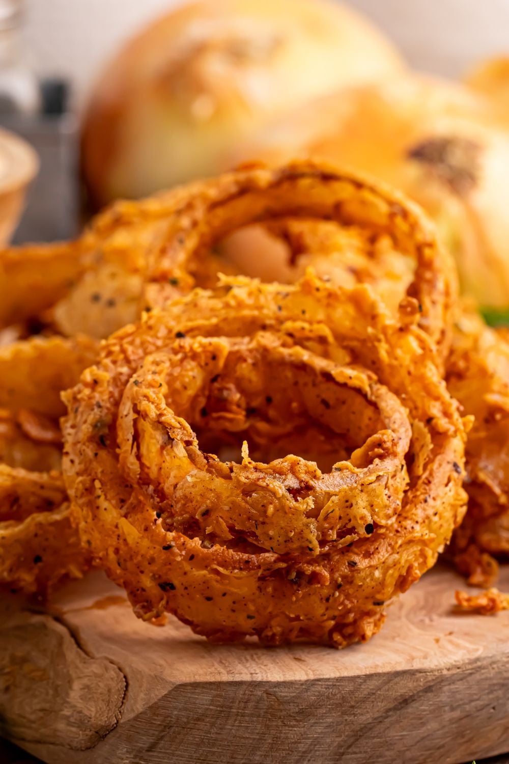 close up look of Homemade Deep Fried Onion Rings on a wooden tray with yellow onions behind it