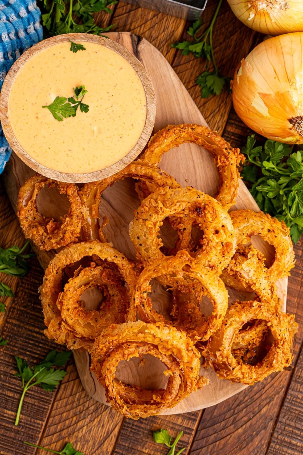 wooden table with a tray with onion rings on top of trya and a bowl of dip to side