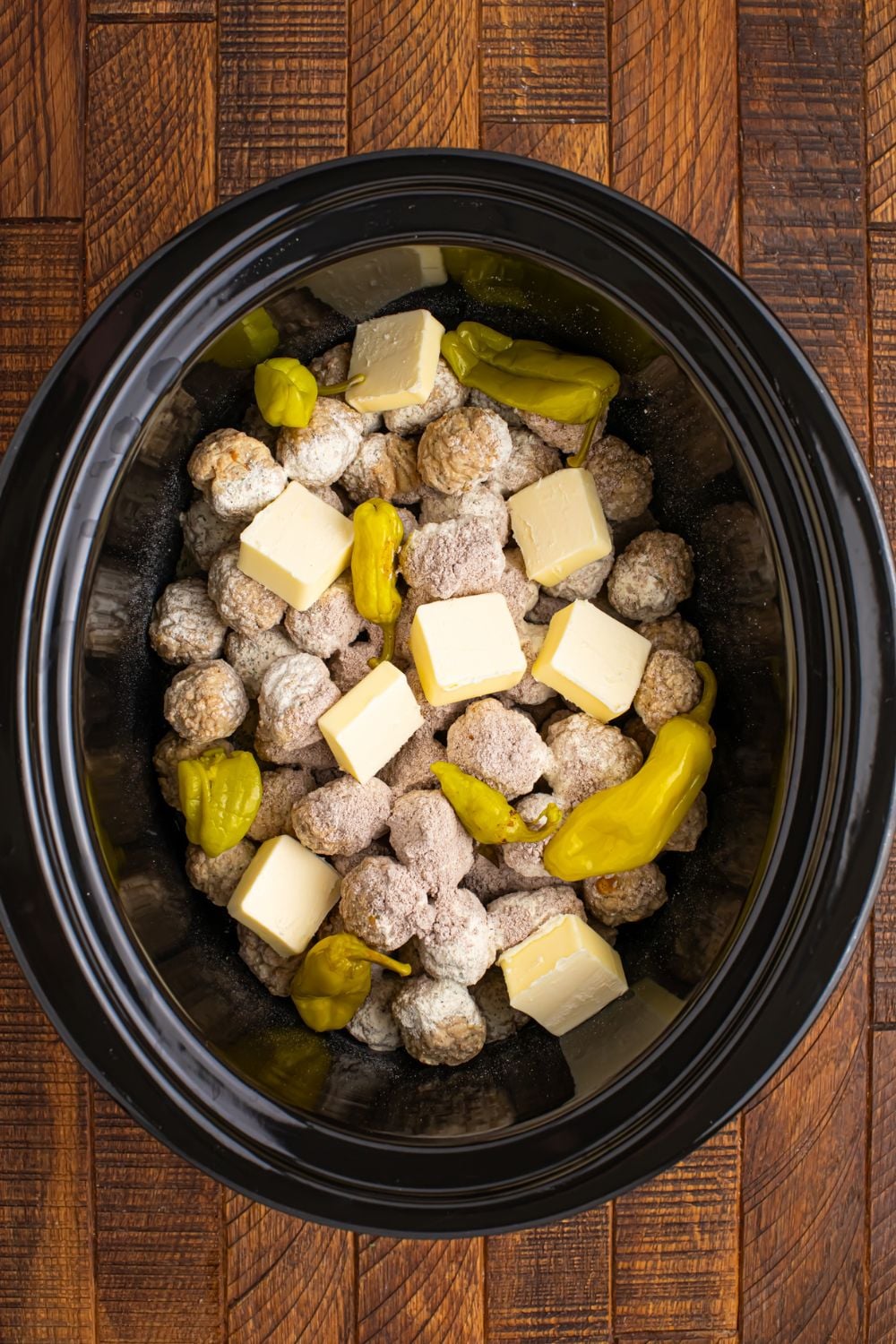 frozen meatballs in a CrockPot with butter and peppers on top