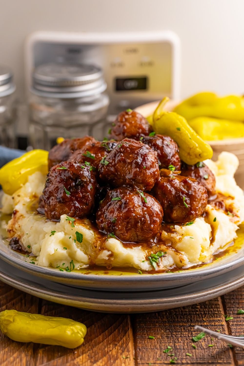 Crockpot Mississippi Meatballs on a stack of plates with more peppers to side and CrockPot behind it on table