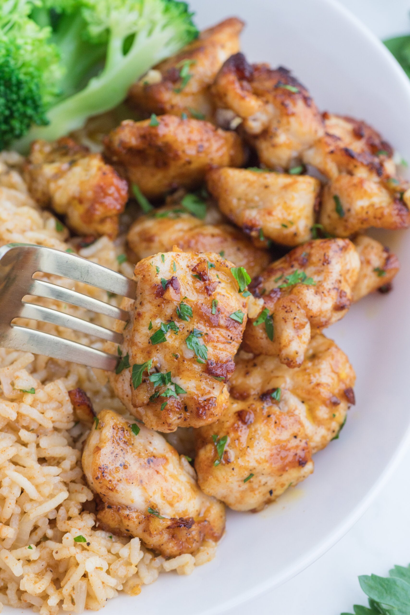 Garlic Butter Chicken Bites on a white plate with a fork lifting one up