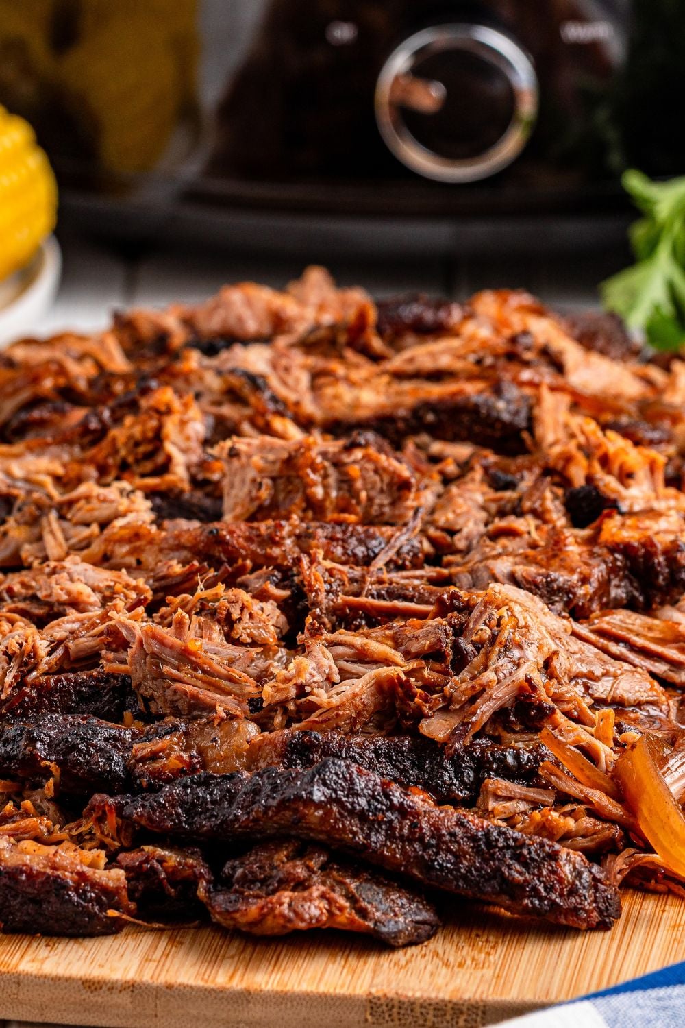 view of a shredded bbq brisket on a cutting board with a slow cooker in the background of image 