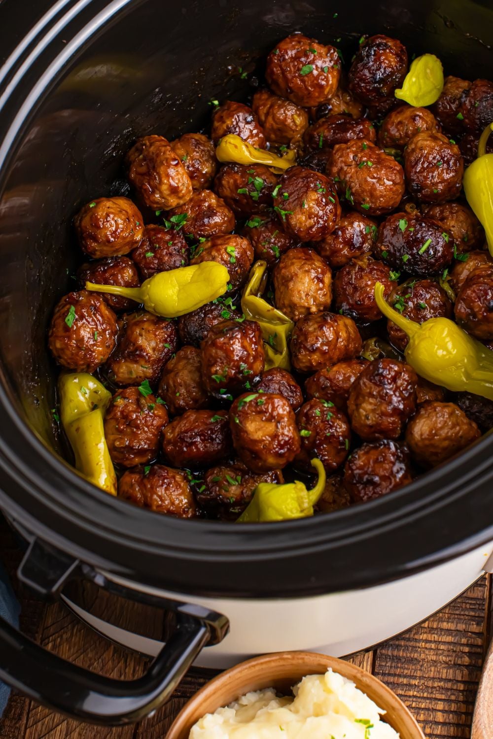 CrockPot angled to side on table with Mississippi meatballs inside and peppers